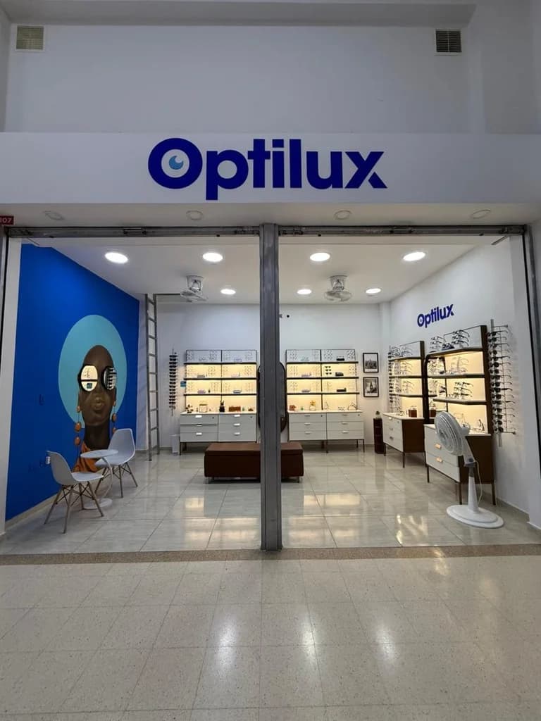 Fachada de entrada de la óptica Optilux Valledupar. Tienda abierta con amplia exhibición de gafas.